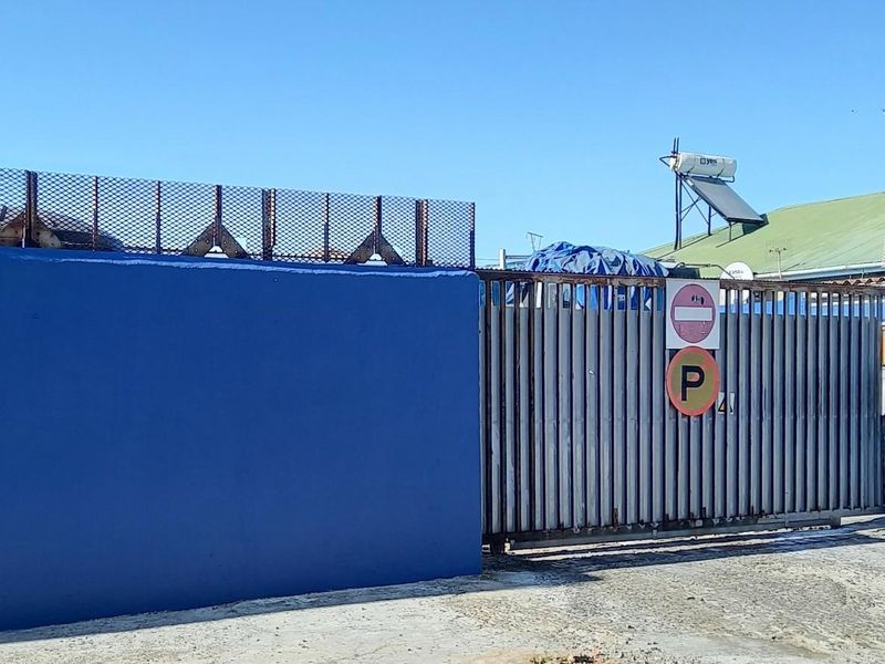 Front exterior view featuring a blue perimeter wall, security mesh fencing, a metal sliding gate, and a solar water heater on the roof.