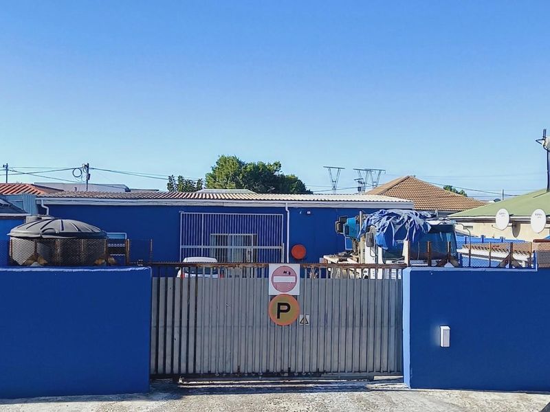Front view of the property featuring a blue perimeter wall, a metal sliding gate, and a solar water heating system on the roof.