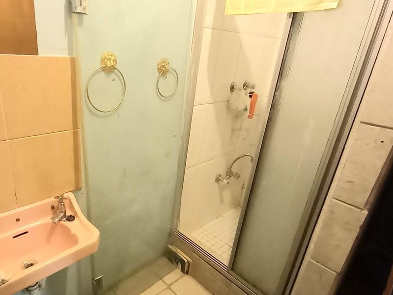 A dated bathroom featuring a pink pedestal basin, a shower enclosure with sliding doors, and tiled wall and floor finishes in need of modernization.