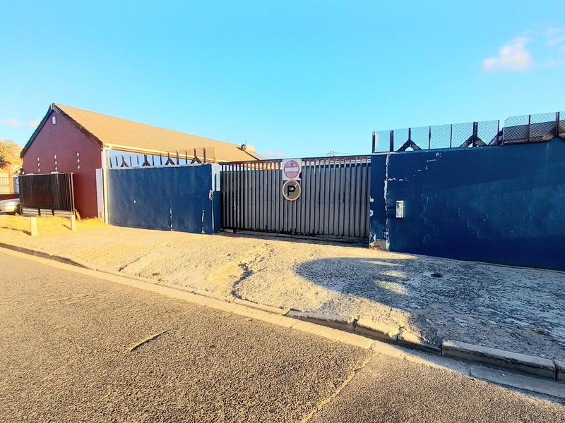 Front exterior view of the property featuring a secure perimeter wall with fencing, a sliding gate, and a paved driveway area.