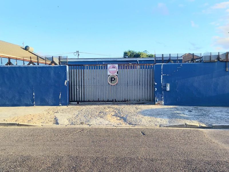 Front exterior view of the property featuring a blue perimeter wall, security fencing, and a metal sliding gate.