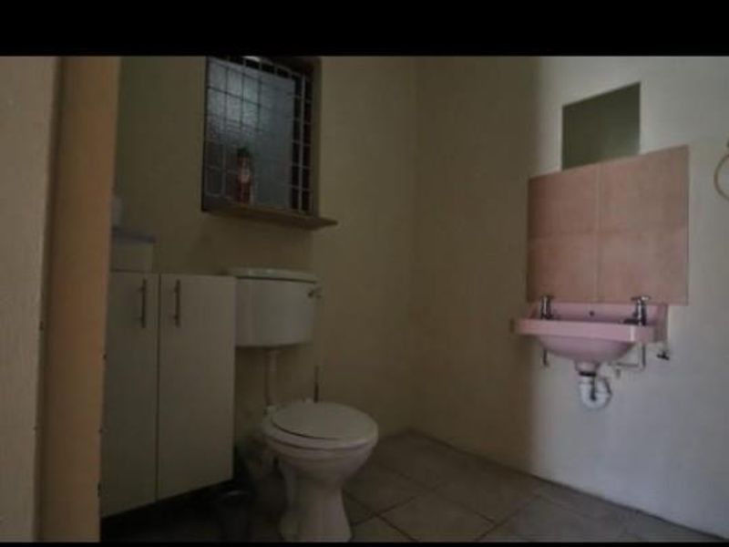 A functional bathroom featuring a toilet, wall-mounted basin with tiled splashback, and a built-in vanity cabinet, requiring cosmetic updates.