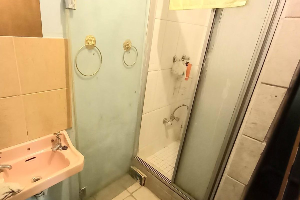 A dated bathroom featuring a pink pedestal basin, a shower enclosure with sliding doors, and tiled wall and floor finishes in need of modernization.