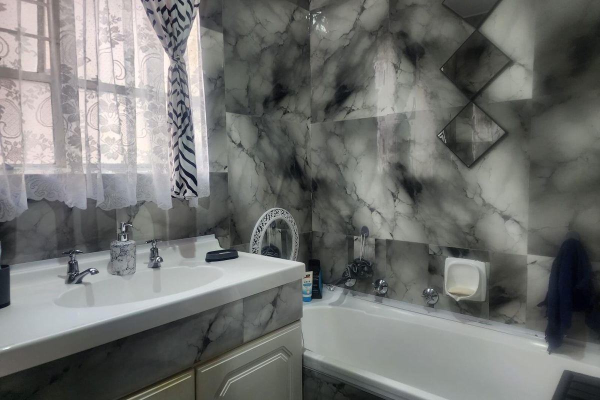 A functional bathroom featuring a built-in bathtub, vanity basin with chrome fixtures, and full-height marble-effect wall tiling.