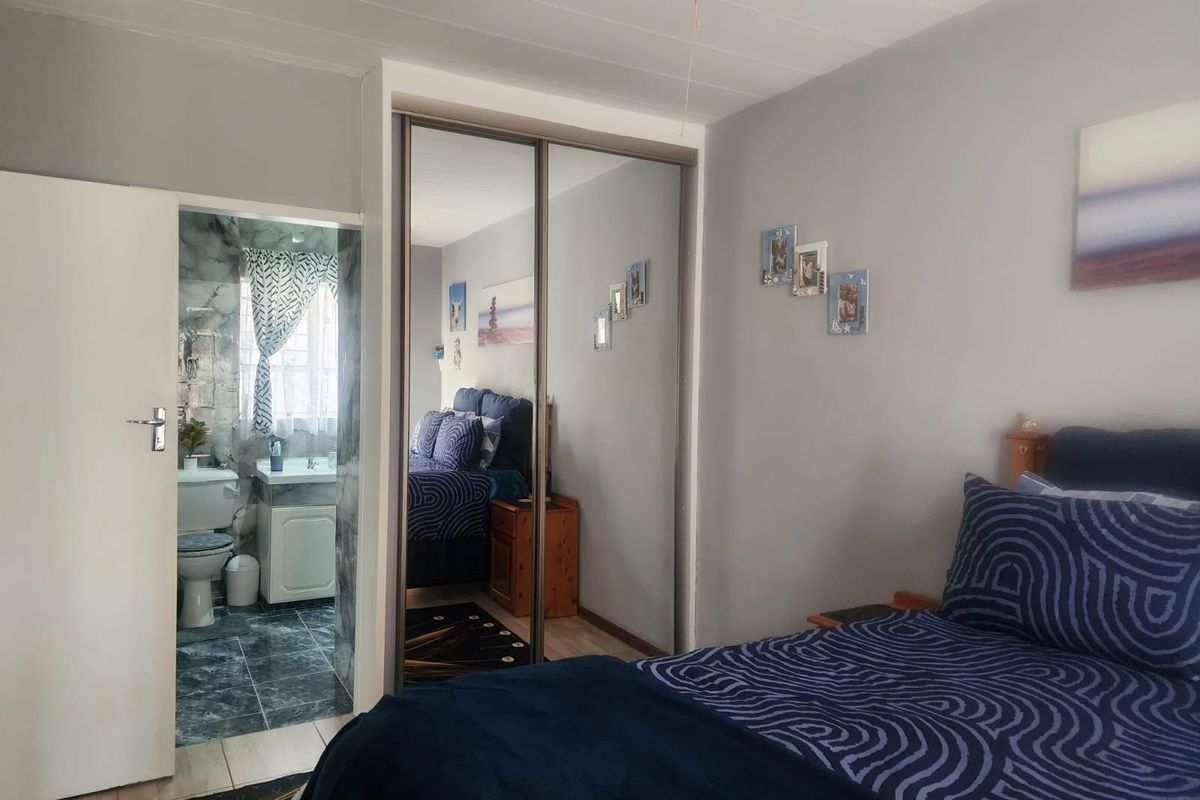 A bedroom featuring built-in mirrored sliding door cupboards and an adjoining en-suite bathroom with tiled flooring.