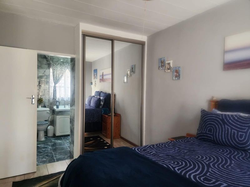 A bedroom featuring built-in mirrored sliding door cupboards and an adjoining en-suite bathroom with tiled flooring.