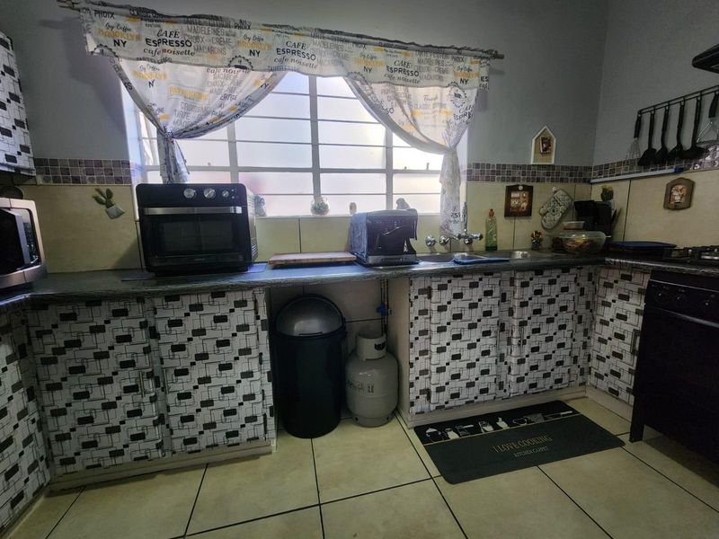 A functional kitchen featuring tiled flooring, a double sink, and built-in cabinetry with a patterned finish, situated beneath a window with security bars.