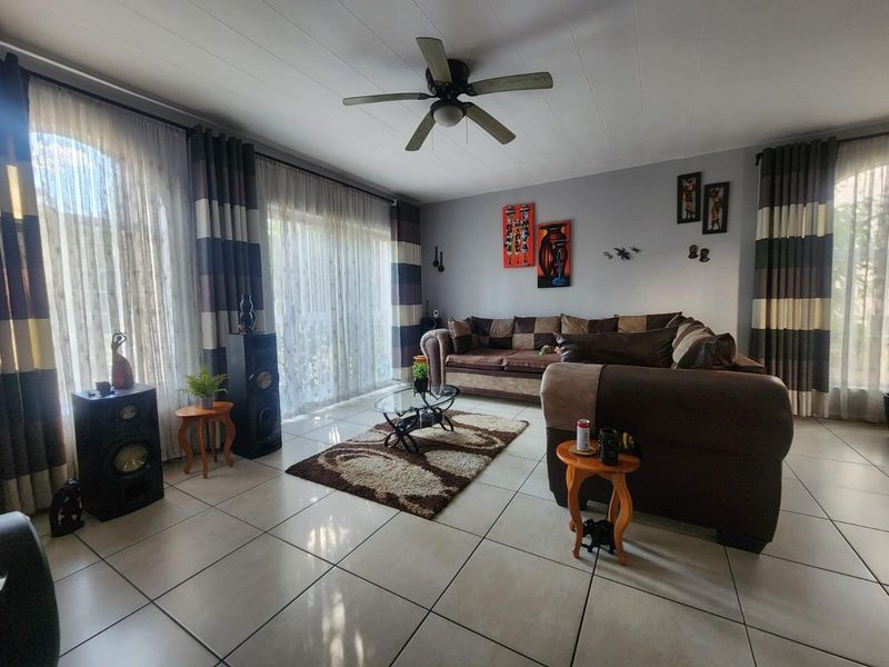 A spacious living room featuring large glass sliding doors, tiled flooring, and a ceiling fan, providing a bright and comfortable living area.