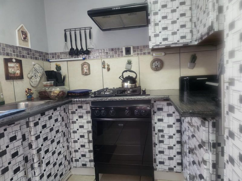 A functional kitchen featuring dark granite countertops, a built-in gas stove with extractor fan, and patterned cabinetry.