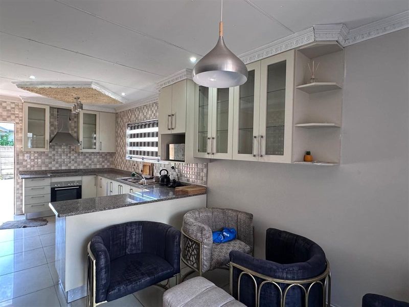 A well-appointed kitchen featuring granite countertops, built-in cabinetry, a stainless steel extractor fan, and a tiled backsplash, seamlessly integrated into an open-plan living space.