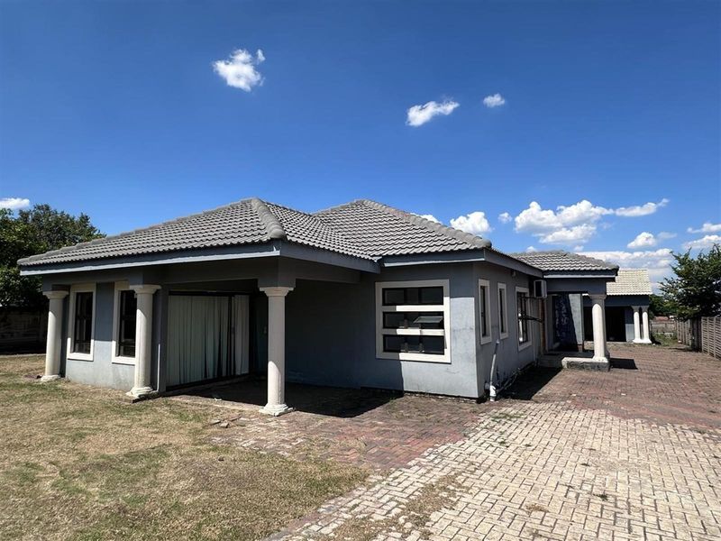 A single-story residential property featuring a tiled roof, decorative columns, and a paved driveway area.