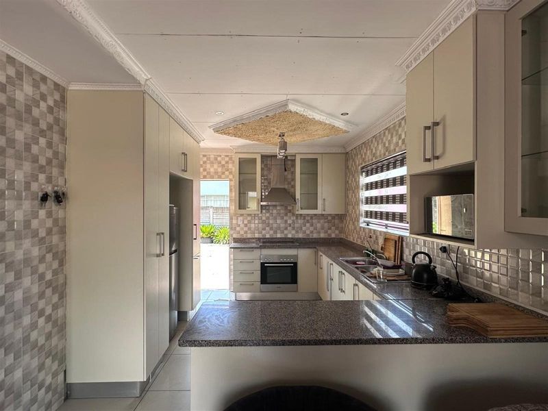 A functional kitchen featuring granite countertops, built-in oven, extractor fan, and tiled splashbacks with direct access to the rear exterior.