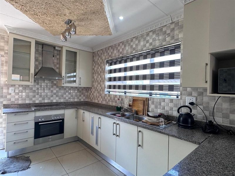 A functional kitchen featuring granite countertops, built-in oven, stainless steel extractor fan, double sink, and tiled splashbacks.