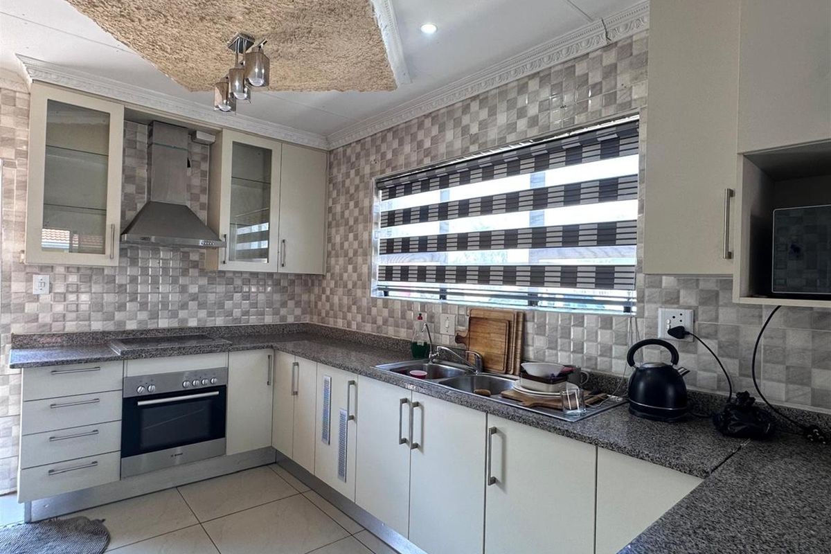 A functional kitchen featuring granite countertops, built-in oven, stainless steel extractor fan, double sink, and tiled splashbacks.