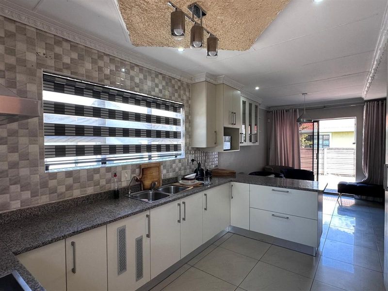 Modern open-plan kitchen featuring granite countertops, sleek white cabinetry, double stainless steel sink, and tiled flooring, seamlessly flowing into the adjacent living area.