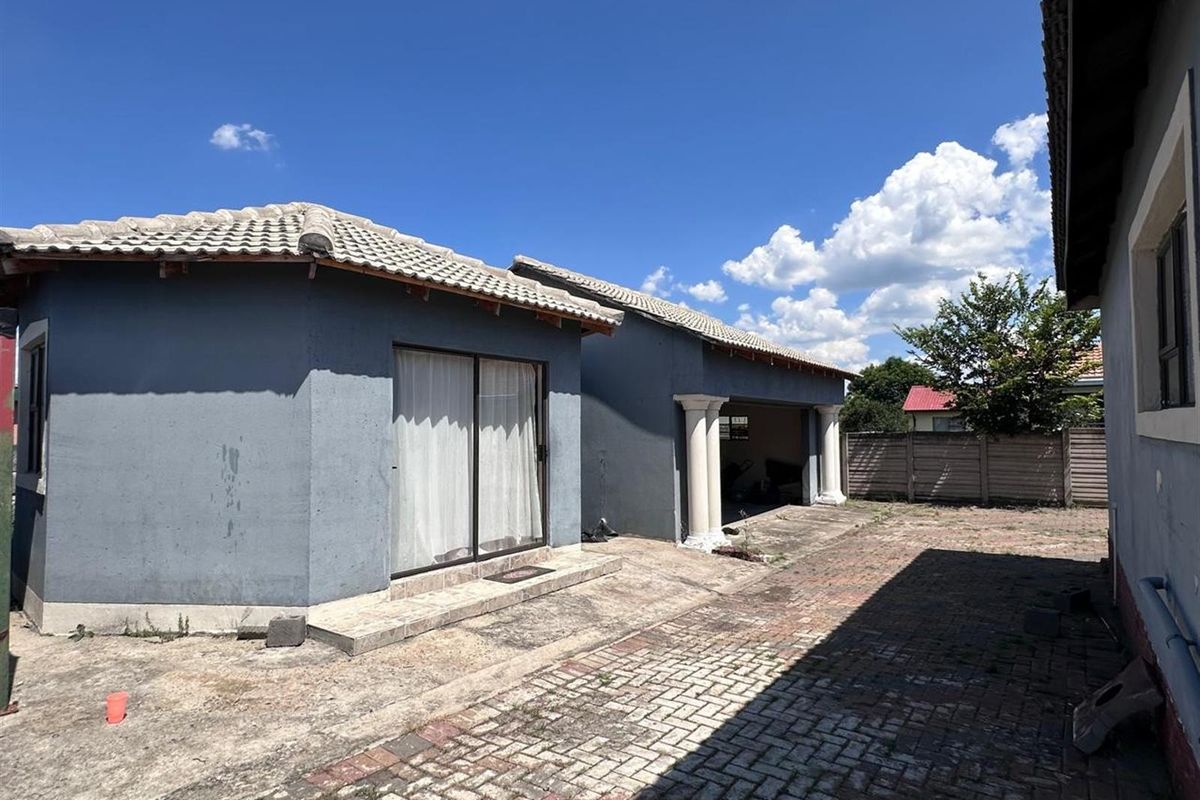 Rear exterior view of the property featuring a paved courtyard, covered patio area with decorative columns, and sliding glass door access.