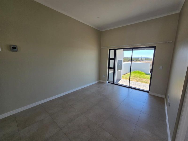 A bright, empty living room featuring neutral walls, large format floor tiles, and a sliding glass door providing access to the rear patio.