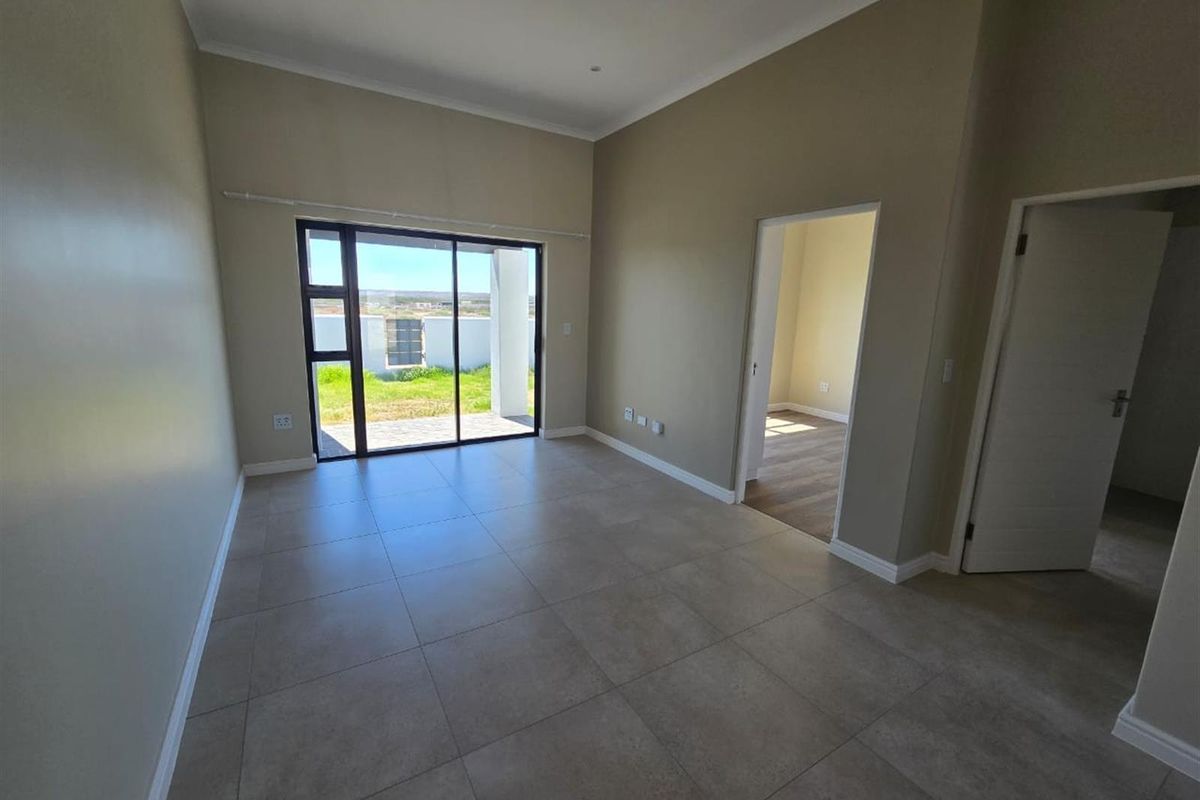 A bright, empty living area featuring large sliding glass doors that open to the exterior, neutral tiled flooring, and recessed lighting.