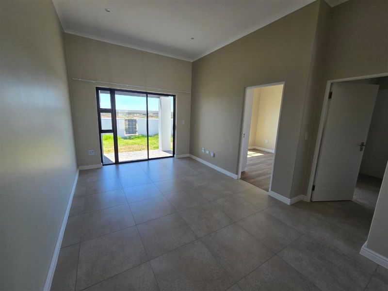 A bright, empty living area featuring large sliding glass doors that open to the exterior, neutral tiled flooring, and recessed lighting.