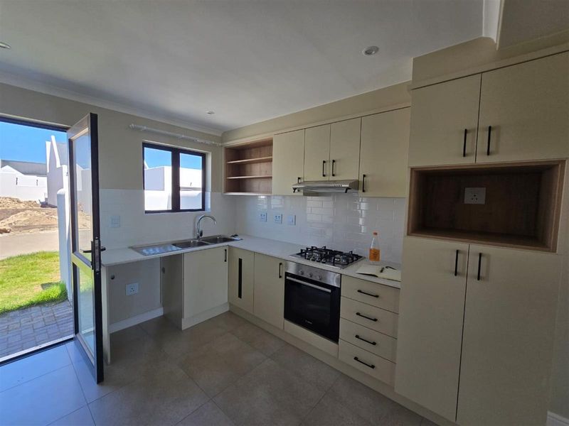 Modern kitchen featuring built-in cabinetry, gas hob, electric oven, extractor fan, and direct access to the exterior through a glass door.