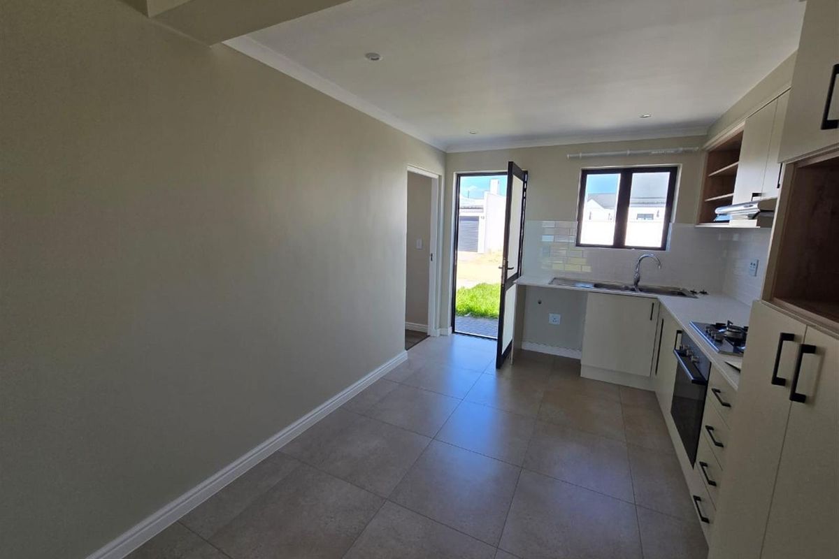 A clean, modern kitchen featuring neutral cabinetry, tiled flooring, built-in oven and hob, and direct access to the exterior.