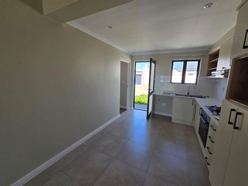 A clean, modern kitchen featuring neutral cabinetry, tiled flooring, built-in oven and hob, and direct access to the exterior.