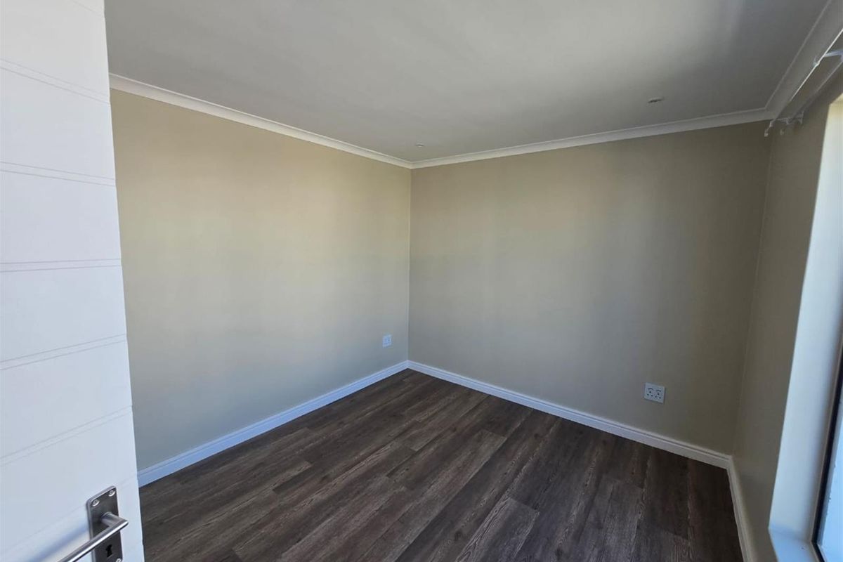 A clean, empty bedroom featuring modern dark laminate flooring, neutral wall paint, and crisp white trim, ready for personalization.