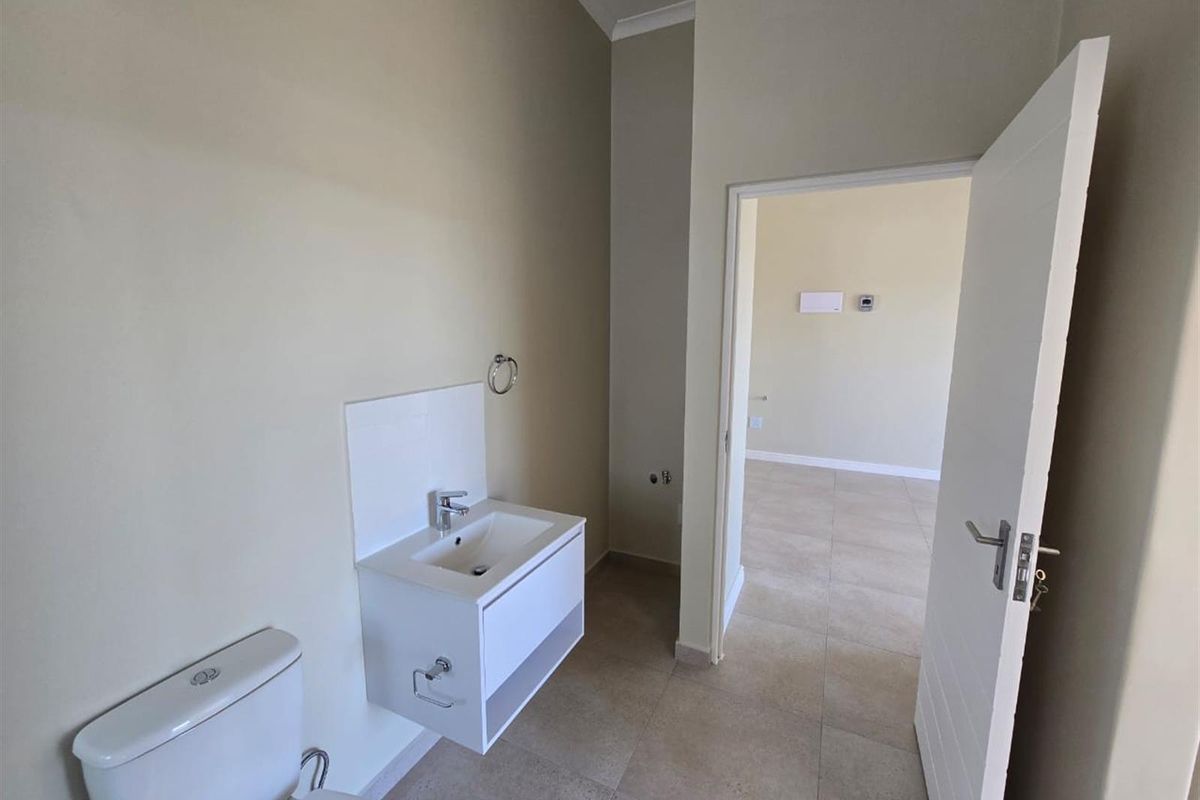 A clean, modern bathroom featuring a wall-mounted vanity with basin, mixer tap, and toilet, finished with neutral wall paint and tiled flooring.