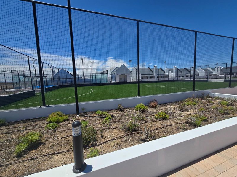 A well-maintained outdoor sports facility featuring artificial turf, perimeter fencing, and integrated floodlighting within a residential estate setting.