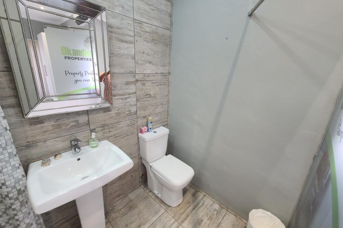 A functional bathroom featuring a pedestal basin, modern toilet, and tiled wall accents with a large decorative mirror.