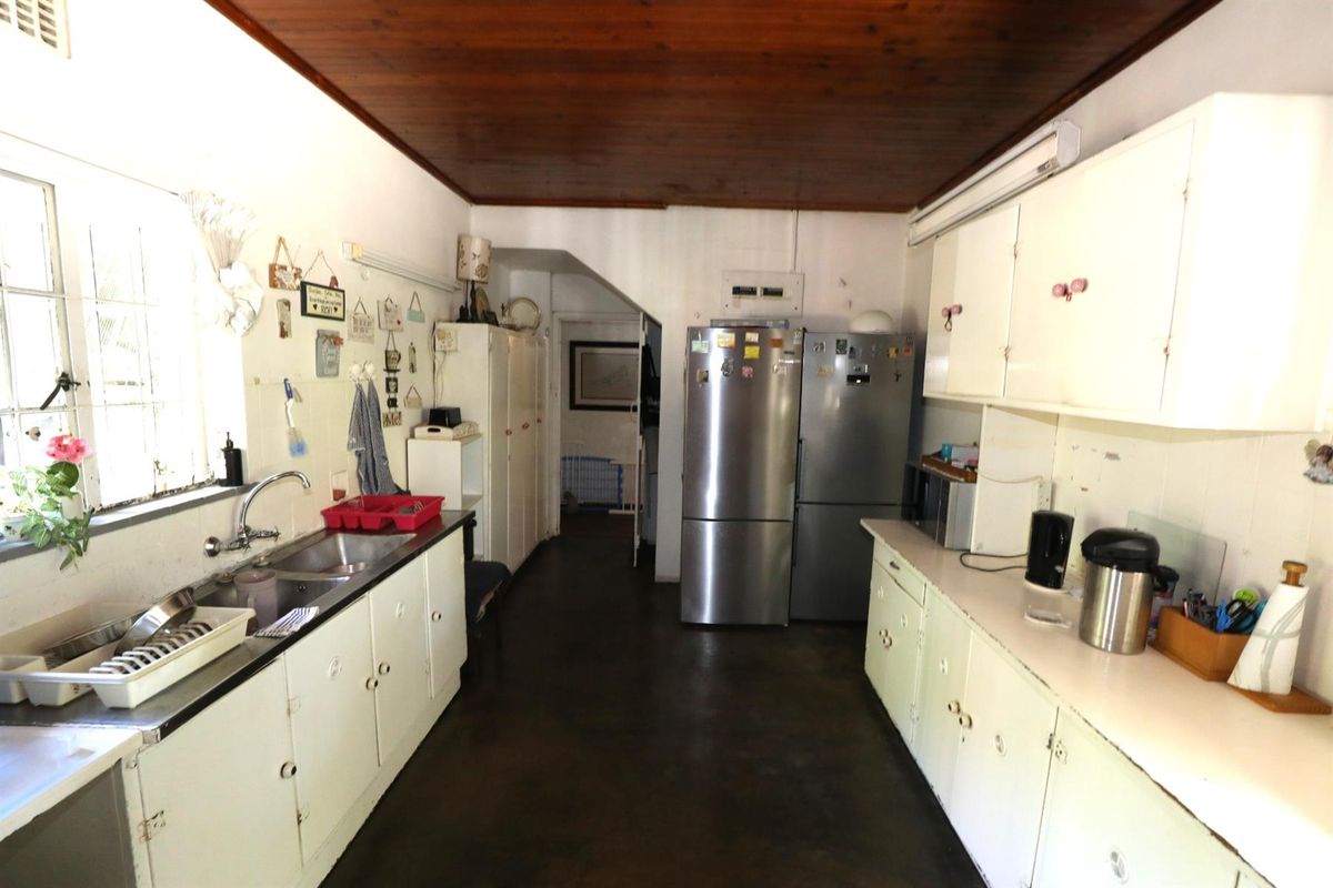 A dated kitchen featuring white cabinetry, a double basin sink, and a timber-paneled ceiling, offering a functional layout with potential for modernization.