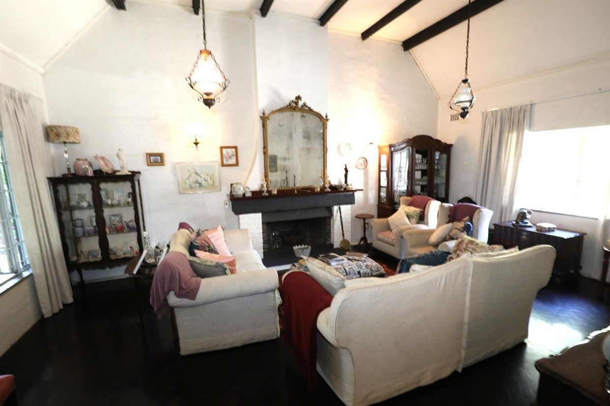 Spacious living room featuring a vaulted ceiling with exposed timber beams, a central fireplace with a mantel, and dark hardwood flooring.