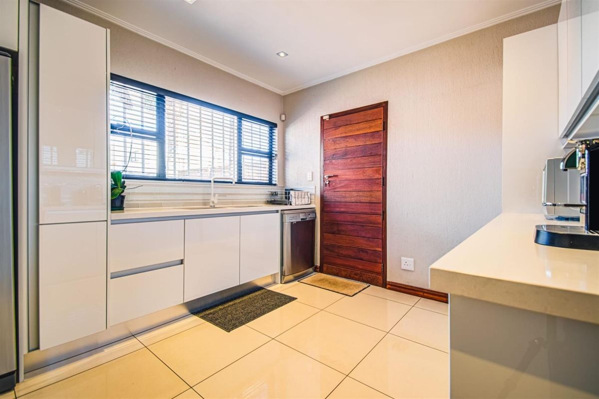 Modern kitchen featuring sleek white cabinetry, stone countertops, tiled flooring, and a solid timber door leading to the exterior.