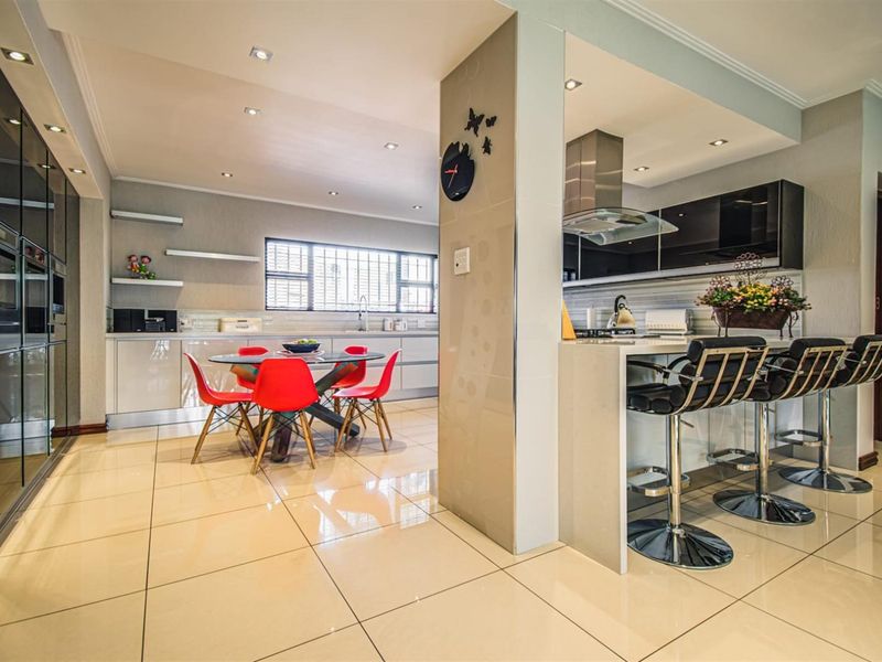 Modern open-plan kitchen and dining area featuring high-gloss cabinetry, integrated appliances, a breakfast bar, and polished tiled flooring with recessed lighting.