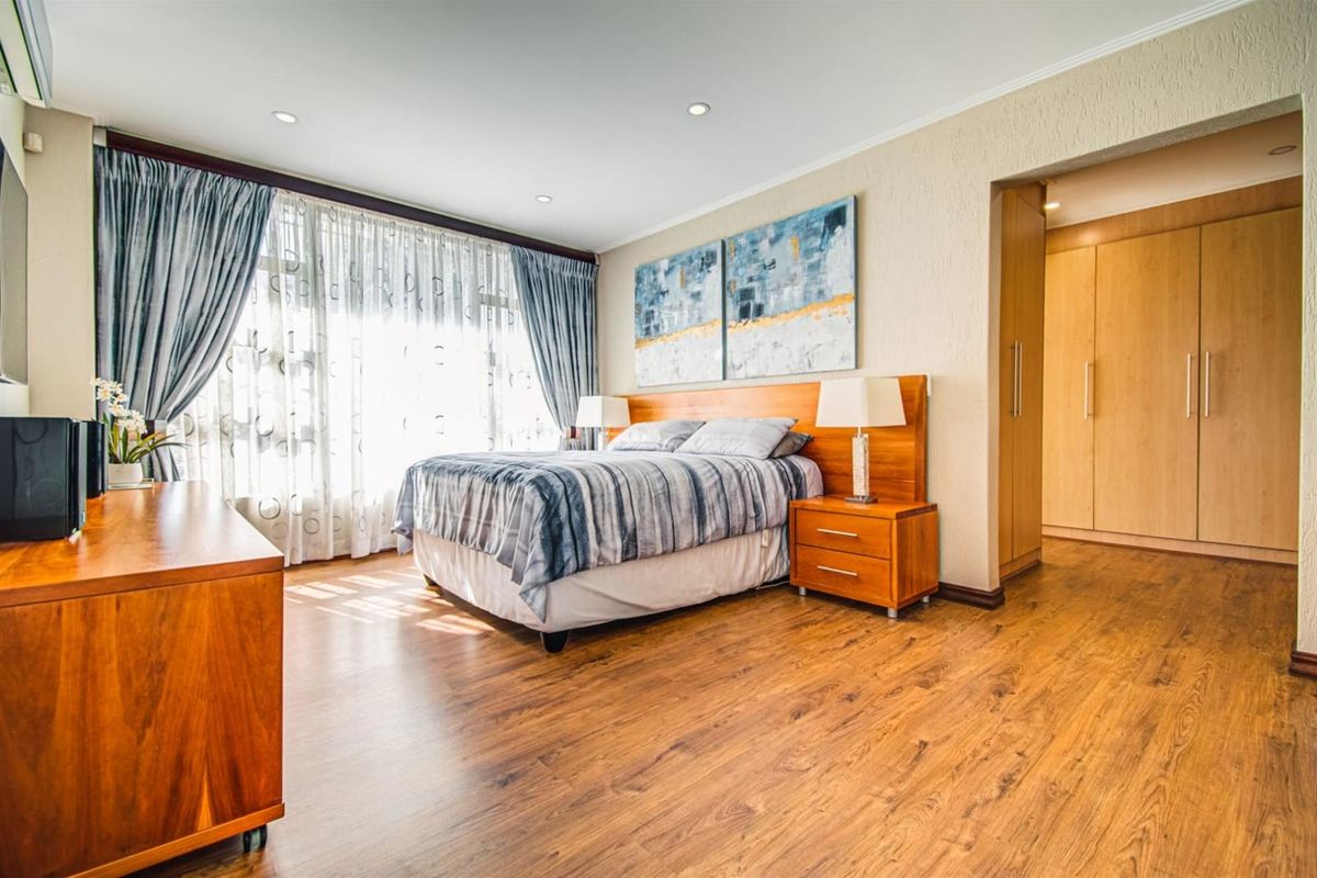 Spacious bedroom featuring warm laminate flooring, recessed downlighting, and extensive built-in cupboard storage with a neutral color palette.