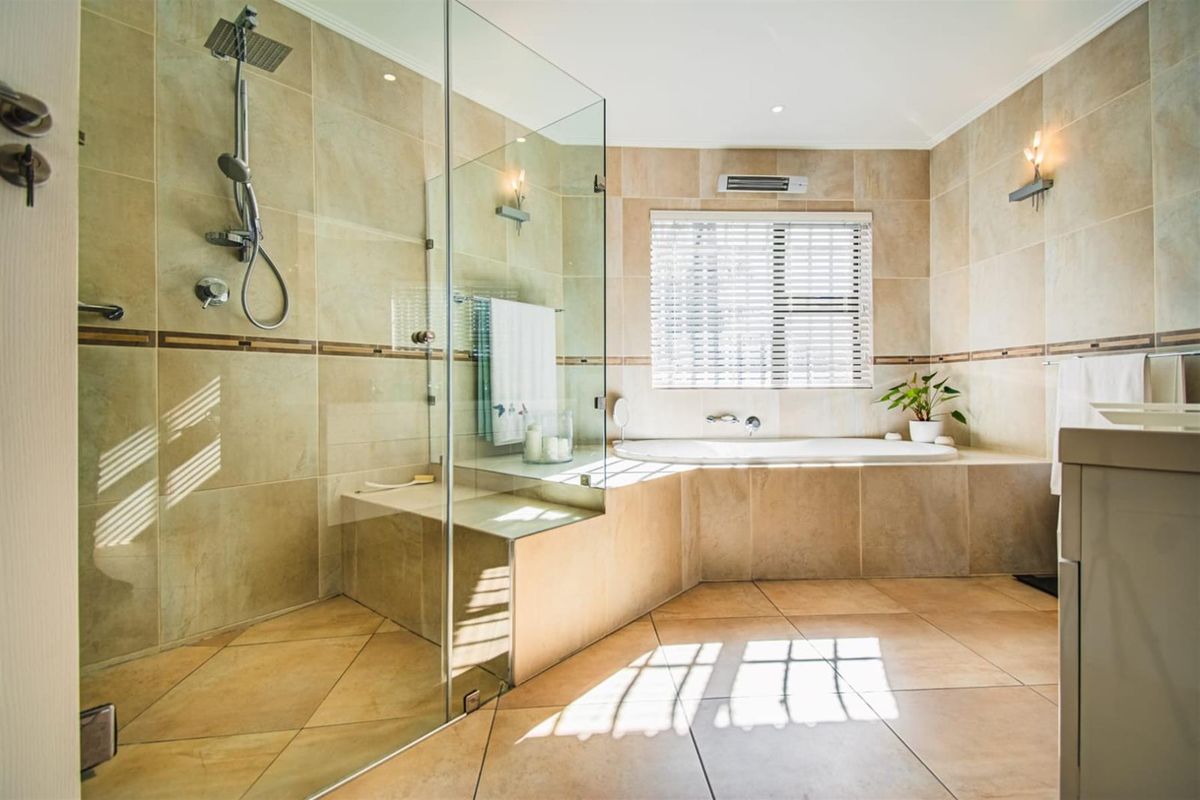 Spacious bathroom featuring a large walk-in shower with glass enclosure, a built-in bathtub, and neutral floor-to-ceiling tiling.