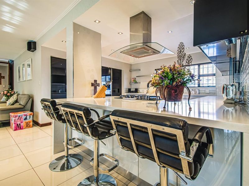 Modern open-plan kitchen featuring a large stone-topped island with breakfast bar seating, integrated gas hob, and stainless steel extractor fan, flowing into the living area.