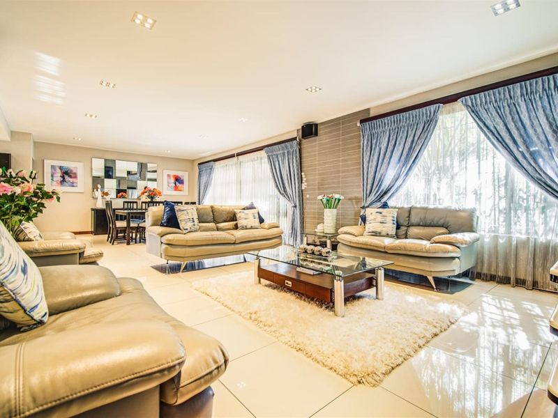 Spacious open-plan living and dining area featuring polished tiled flooring, recessed lighting, and a textured feature wall with large windows.