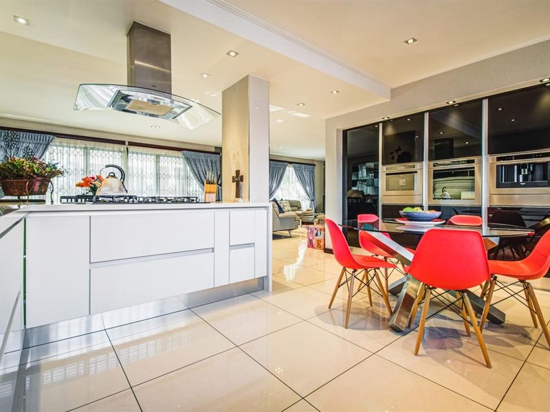 Modern open-plan kitchen and dining area featuring a central island with gas cooktop, integrated appliances, sleek cabinetry, and polished tiled flooring.