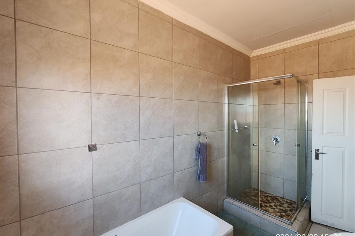 A functional bathroom featuring a built-in bathtub, a separate glass-enclosed shower, and neutral wall tiling throughout.