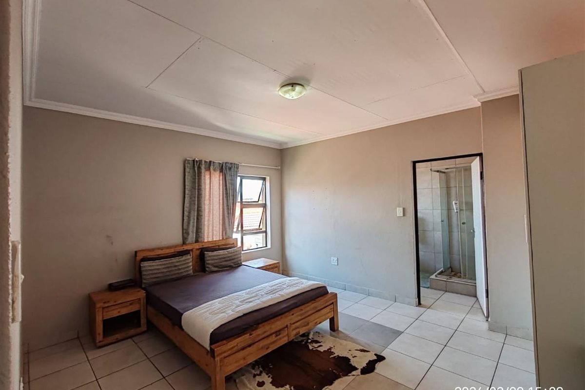 A bedroom featuring tiled flooring, a ceiling-mounted light fixture, and an en-suite bathroom with a glass-enclosed shower.