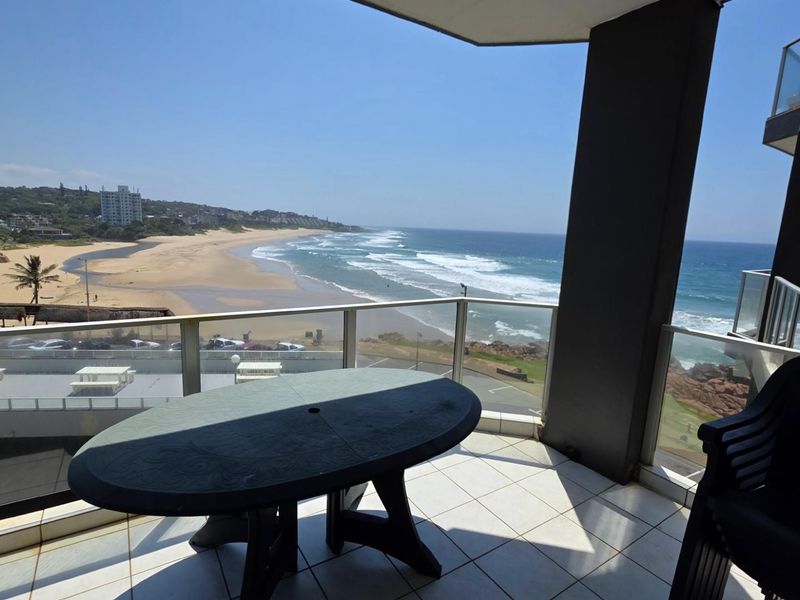 A spacious balcony featuring tiled flooring and a glass balustrade, offering panoramic views of the coastline and ocean.