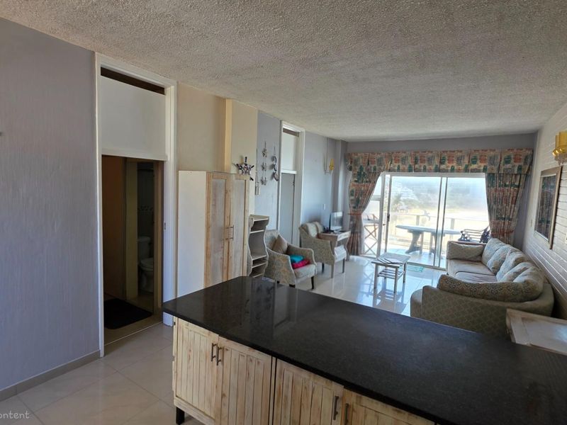 Open plan living area featuring a kitchen island with granite countertop, tiled flooring, and sliding glass doors leading to a balcony with coastal views.