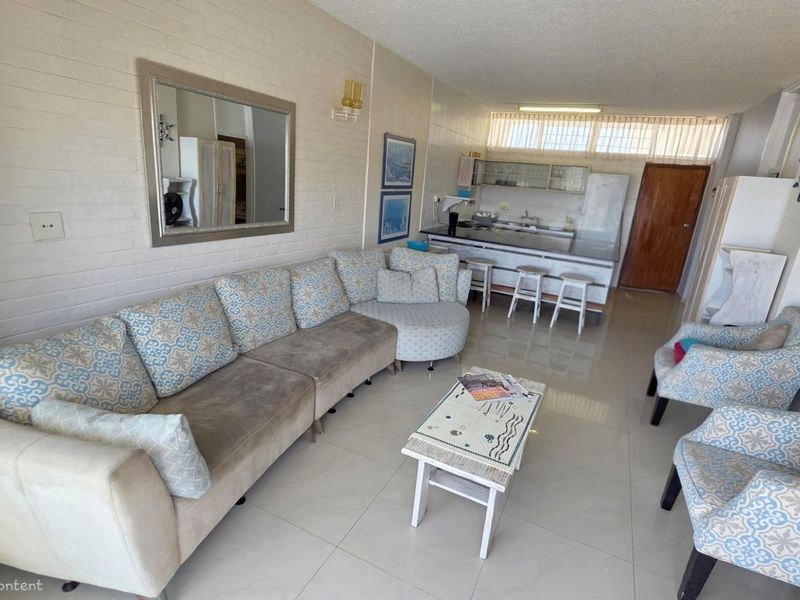 Open-plan living area featuring a kitchen with breakfast bar, tiled flooring, and a textured feature wall, creating a functional and connected living space.
