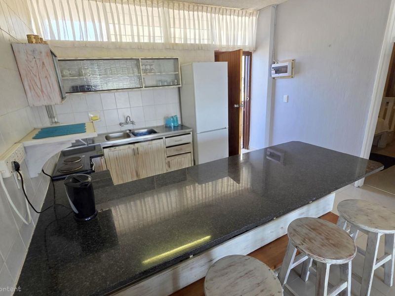 Kitchen area featuring a dark granite breakfast bar, built-in cabinetry, stainless steel sink, and tiled wall finishes.