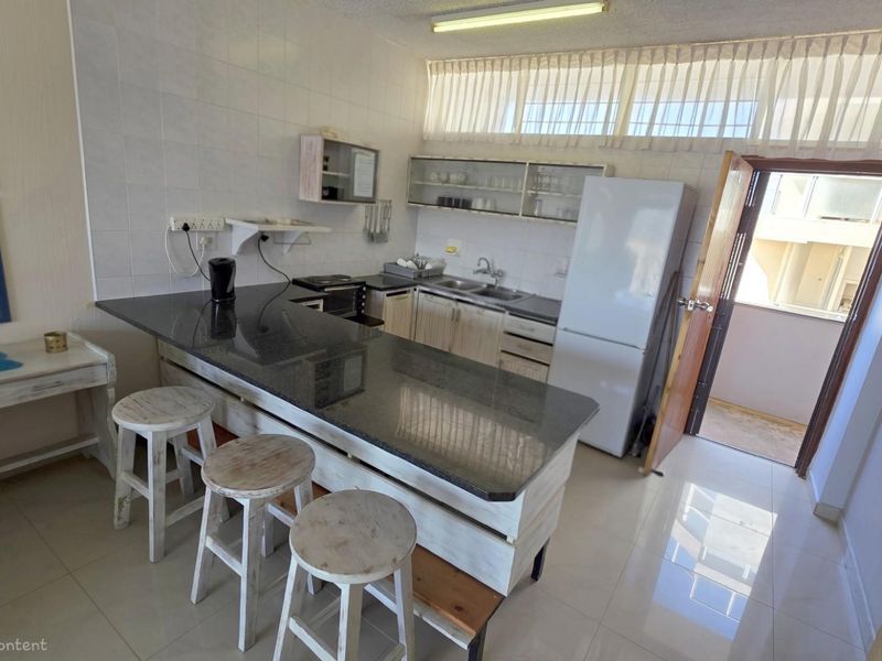 A functional kitchen featuring a granite-topped breakfast bar, tiled flooring, and direct access to an outdoor balcony area.