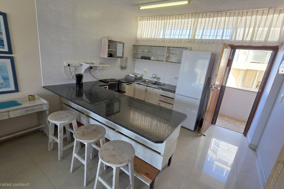 A functional kitchen featuring a granite-topped breakfast bar, tiled flooring, and direct access to an outdoor balcony area.