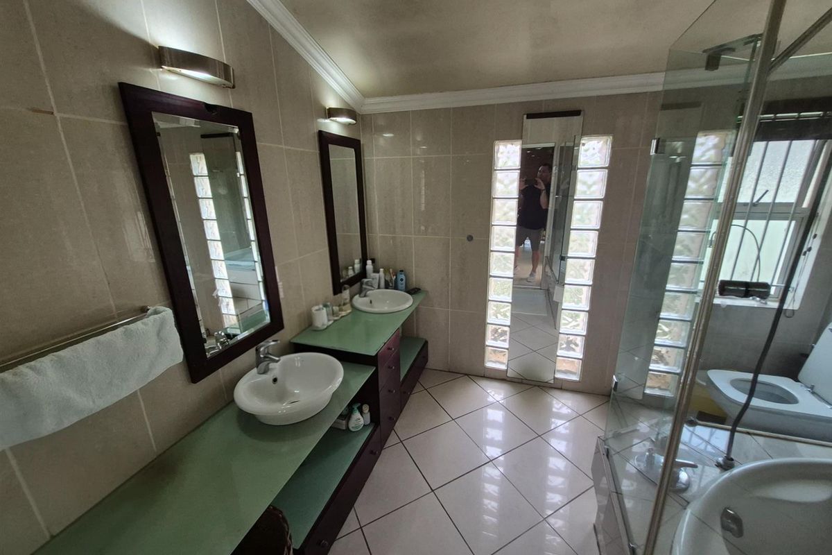 A bathroom featuring a double vanity with glass countertops, a glass-enclosed shower, and glass block wall accents.