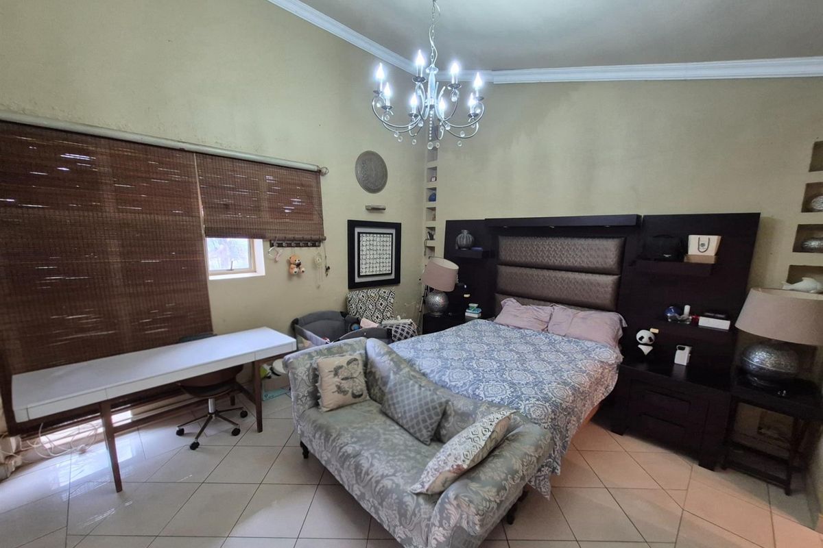 Spacious bedroom featuring tiled flooring, a built-in headboard with integrated shelving, and a decorative chandelier.