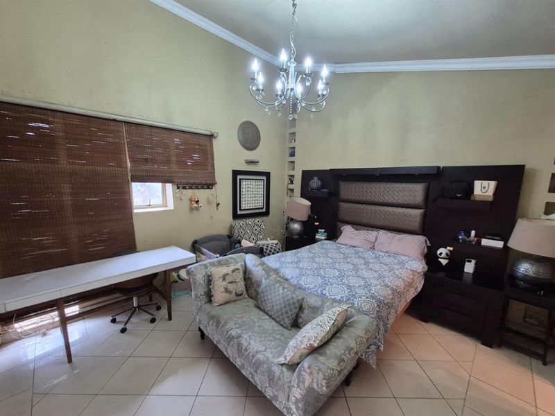 Spacious bedroom featuring tiled flooring, a built-in headboard with integrated shelving, and a decorative chandelier.